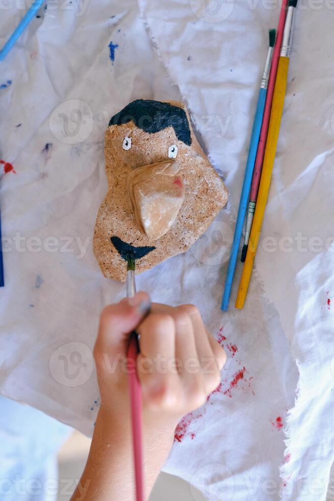 Unrecognizable child painting stone with gouache photo