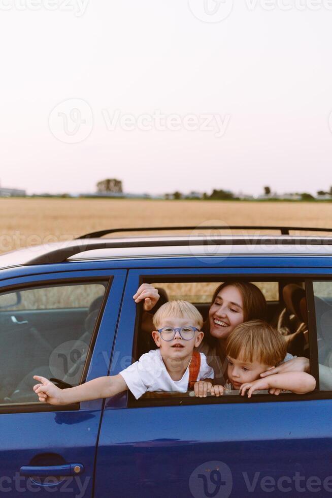 Young woman with little sons sitting in car in countryside photo