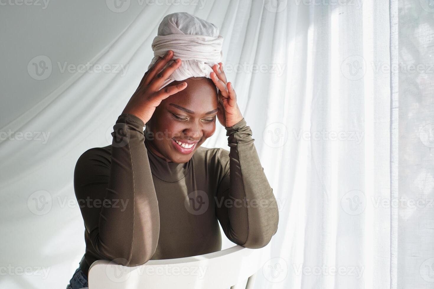 Cheerful woman in white turban touching head and looking down photo