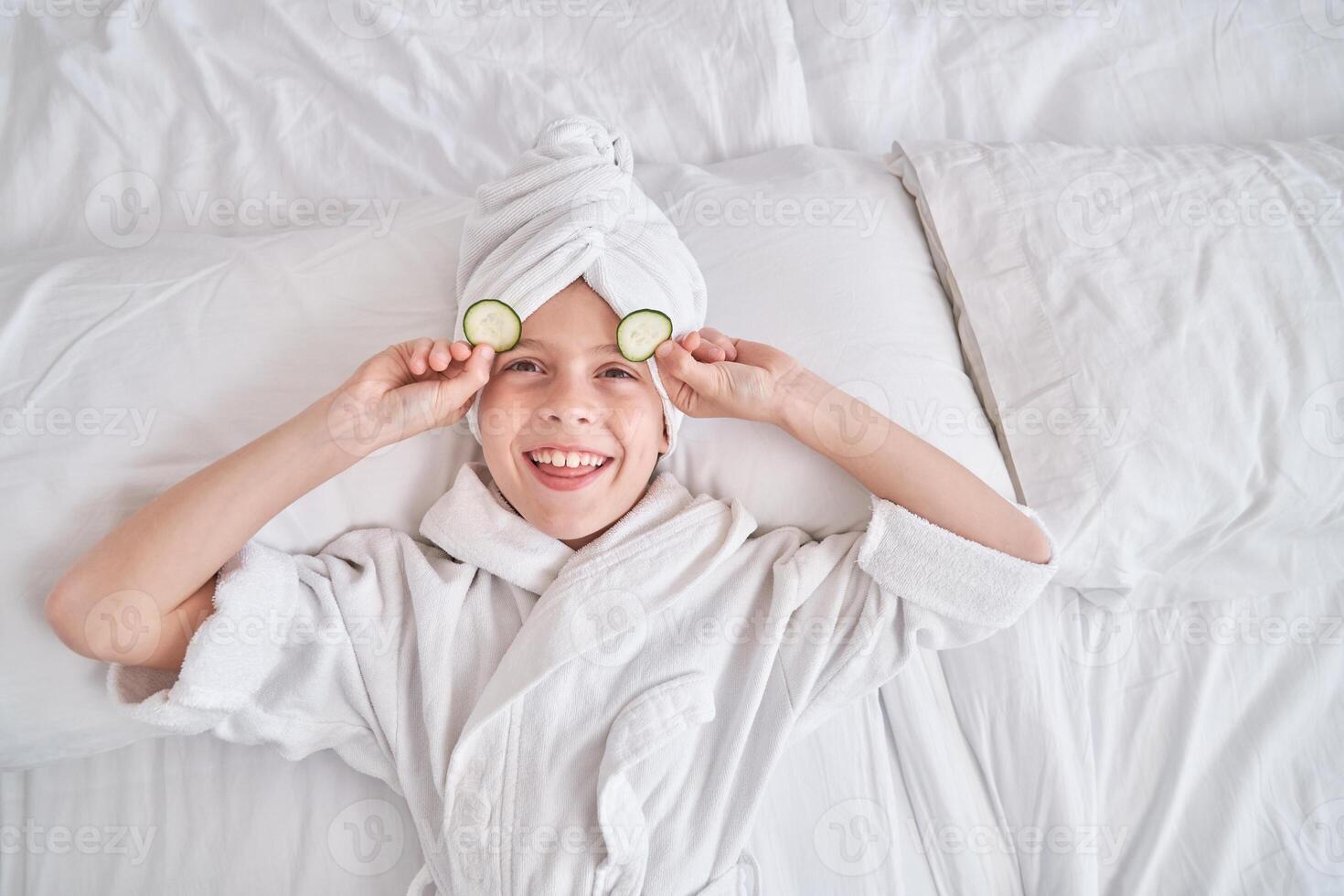 Boy taking off cucumber slices from eyes during spa procedures photo