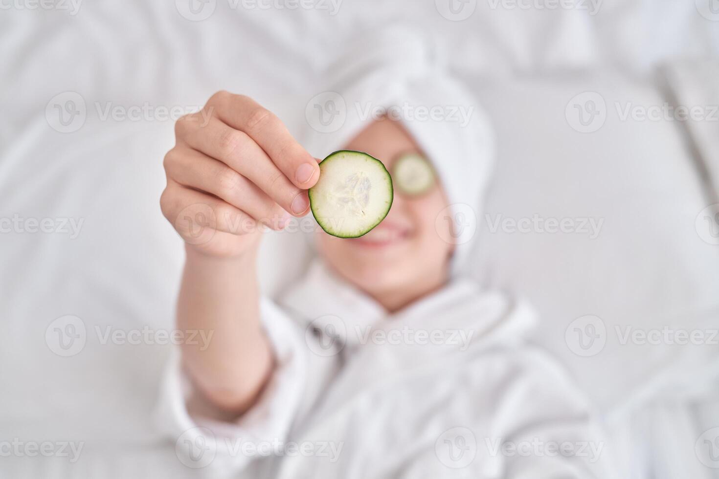 Boy demonstrating cucumber slice and relaxing at home photo