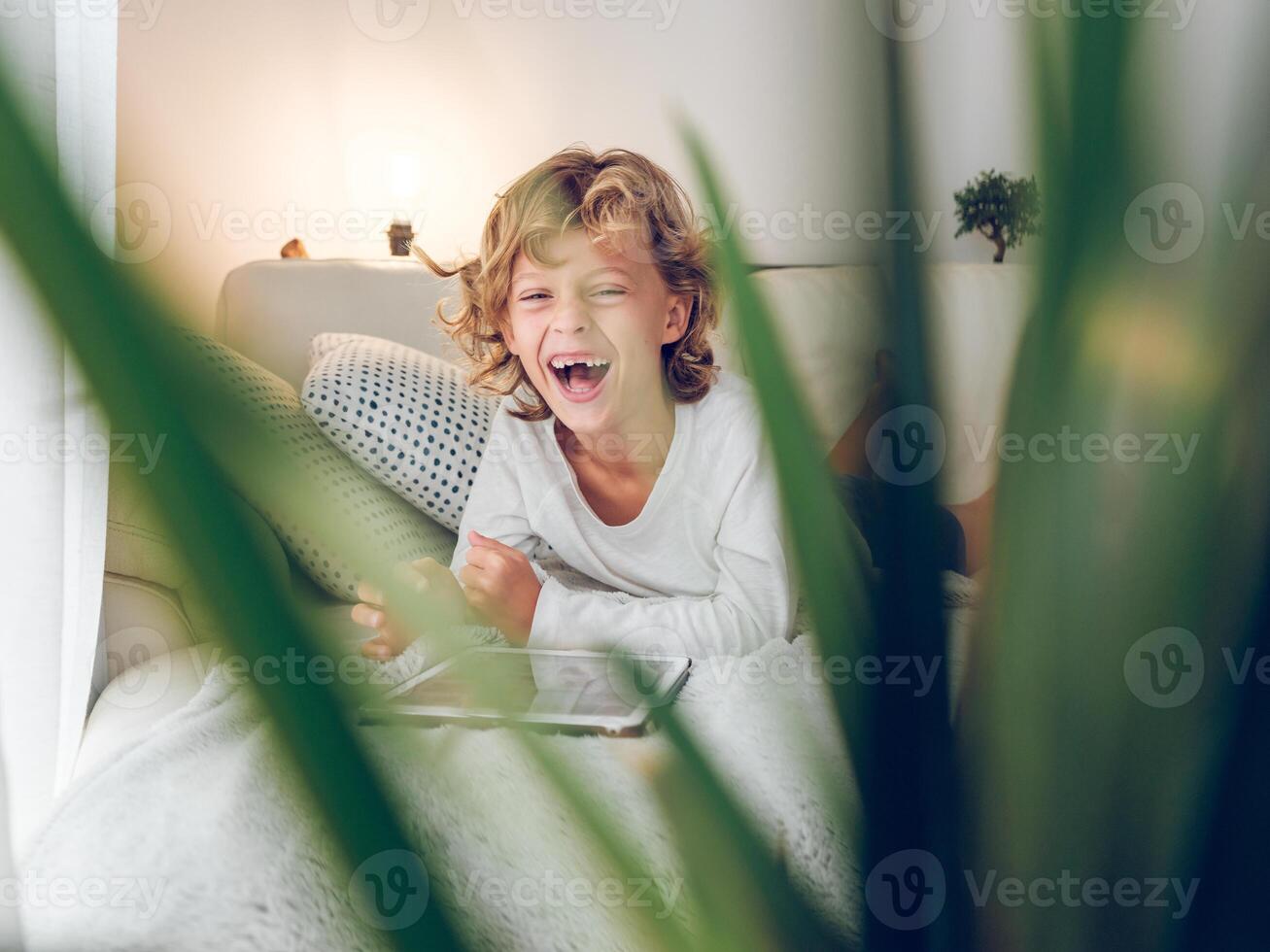 Excited boy lying on sofa watching on tablet photo