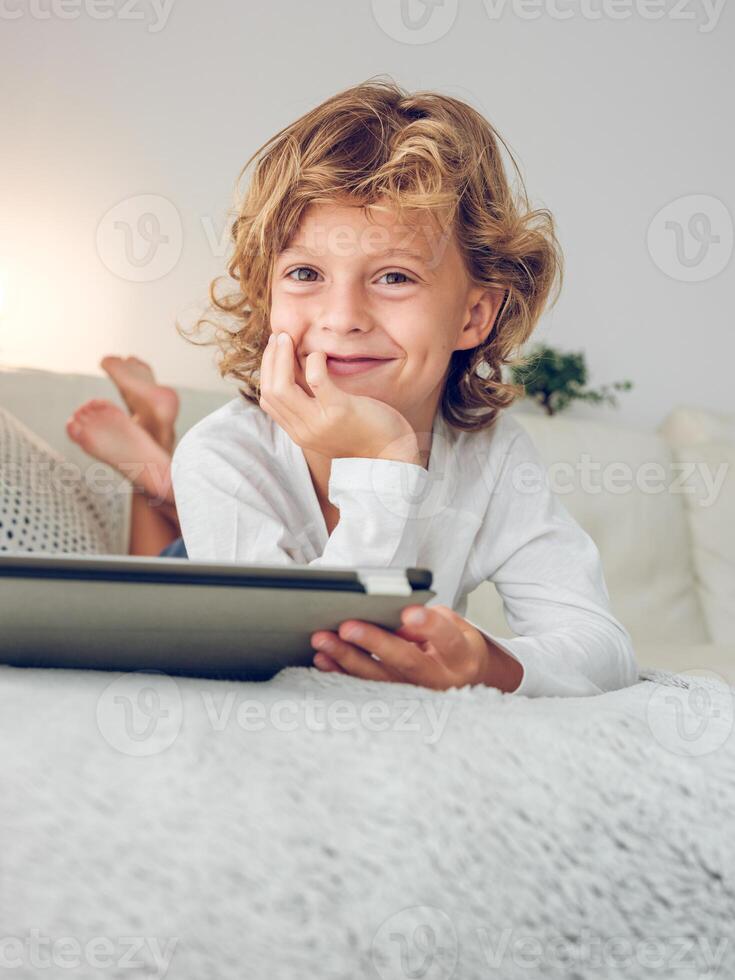 Charming preteen boy with tablet lying on sofa photo