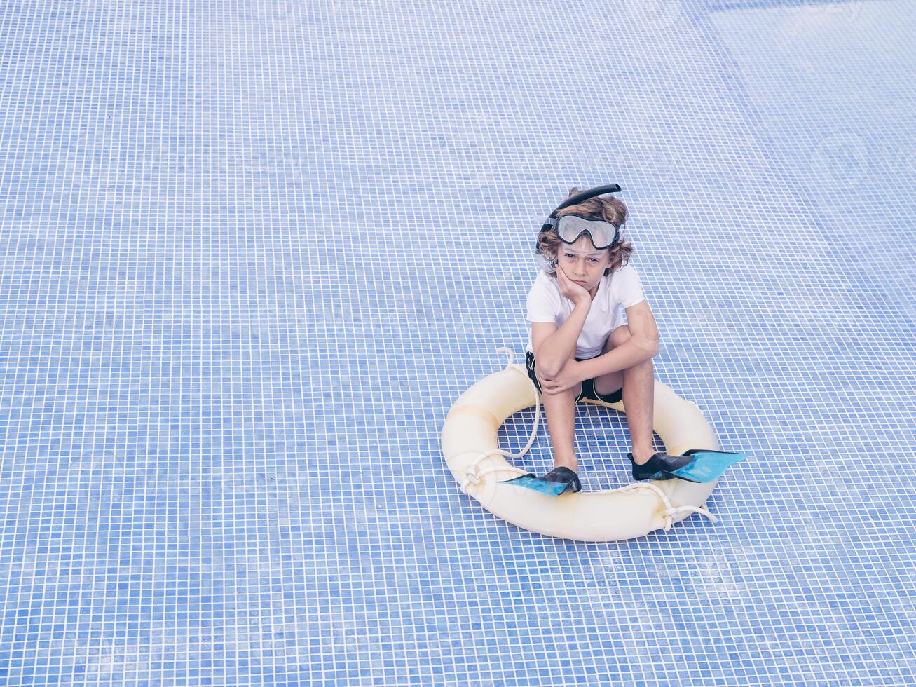Upset kid with swimming tools on bottom of empty pool photo