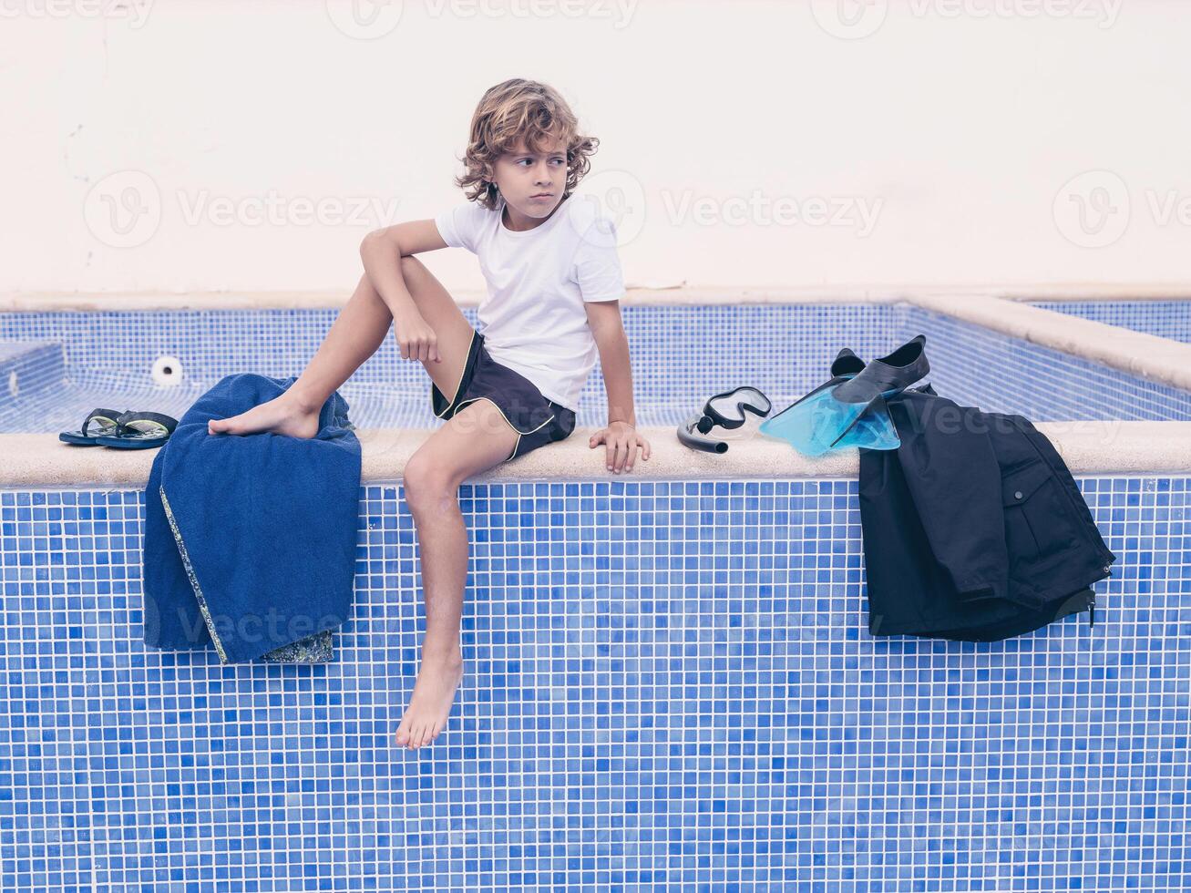 Blond boy with swimming equipment near pool photo