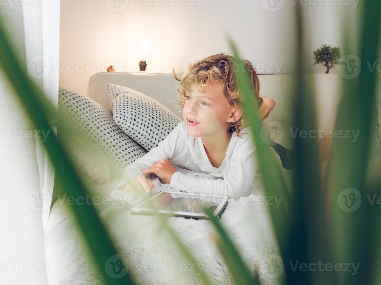 Cute boy on sofa with tablet looking at window photo