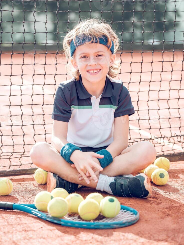 Content kid tennis player resting on court and smiling after mat photo