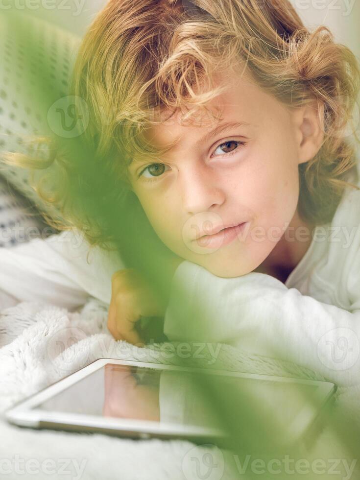 Charming preteen boy lying with tablet and looking at camera photo