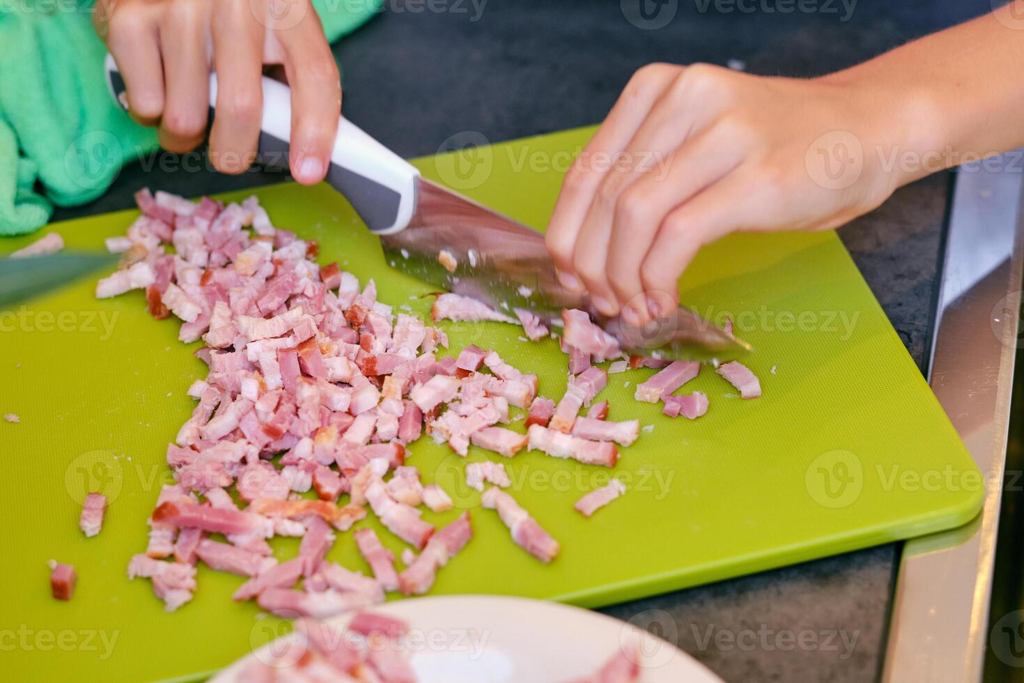 Crop person cutting smoked bacon while cooking in kitchen photo