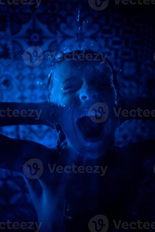 Shirtless boy shouting in shower room in blue light photo