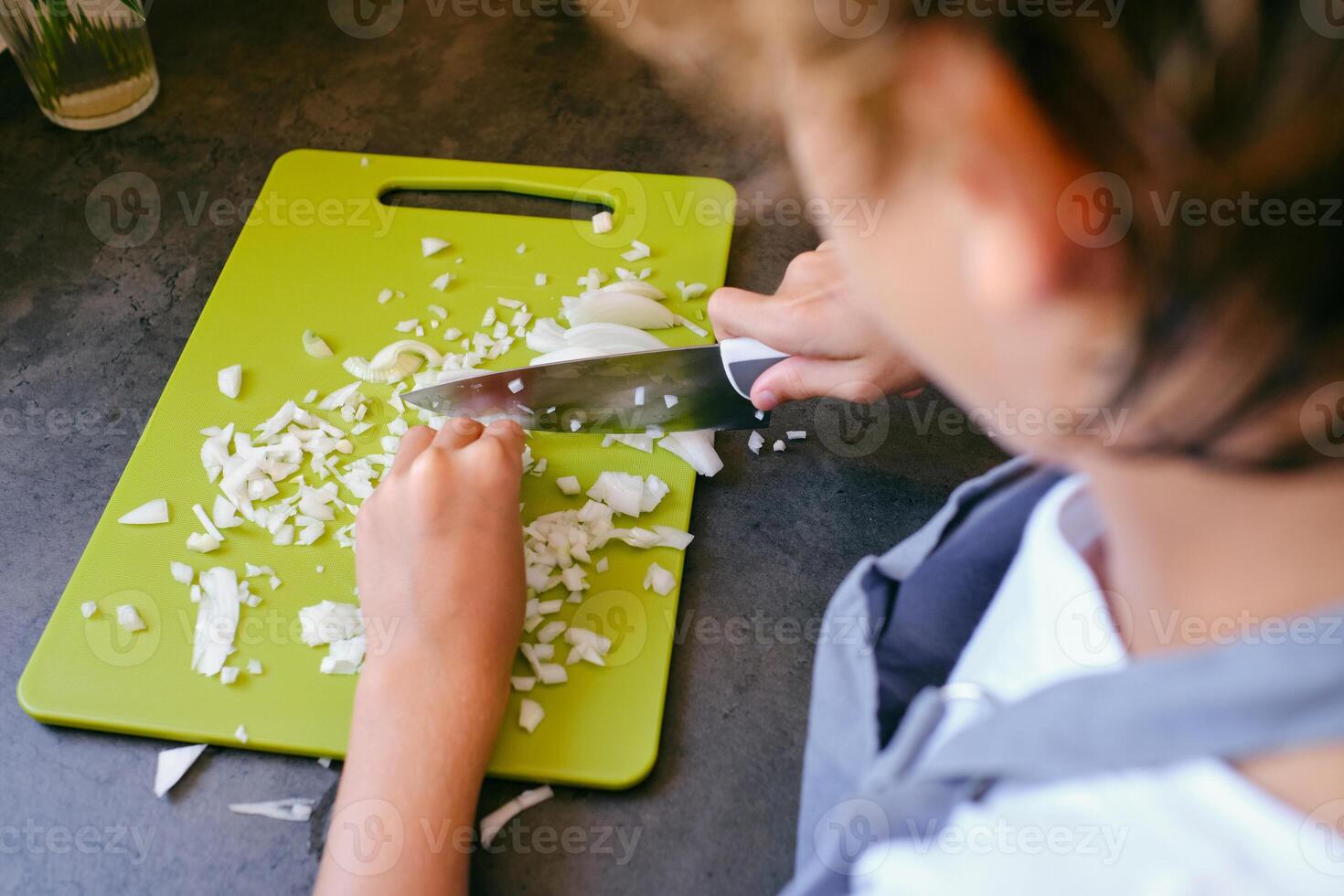 Crop boy chopping fresh onion while cooking in kitchen photo