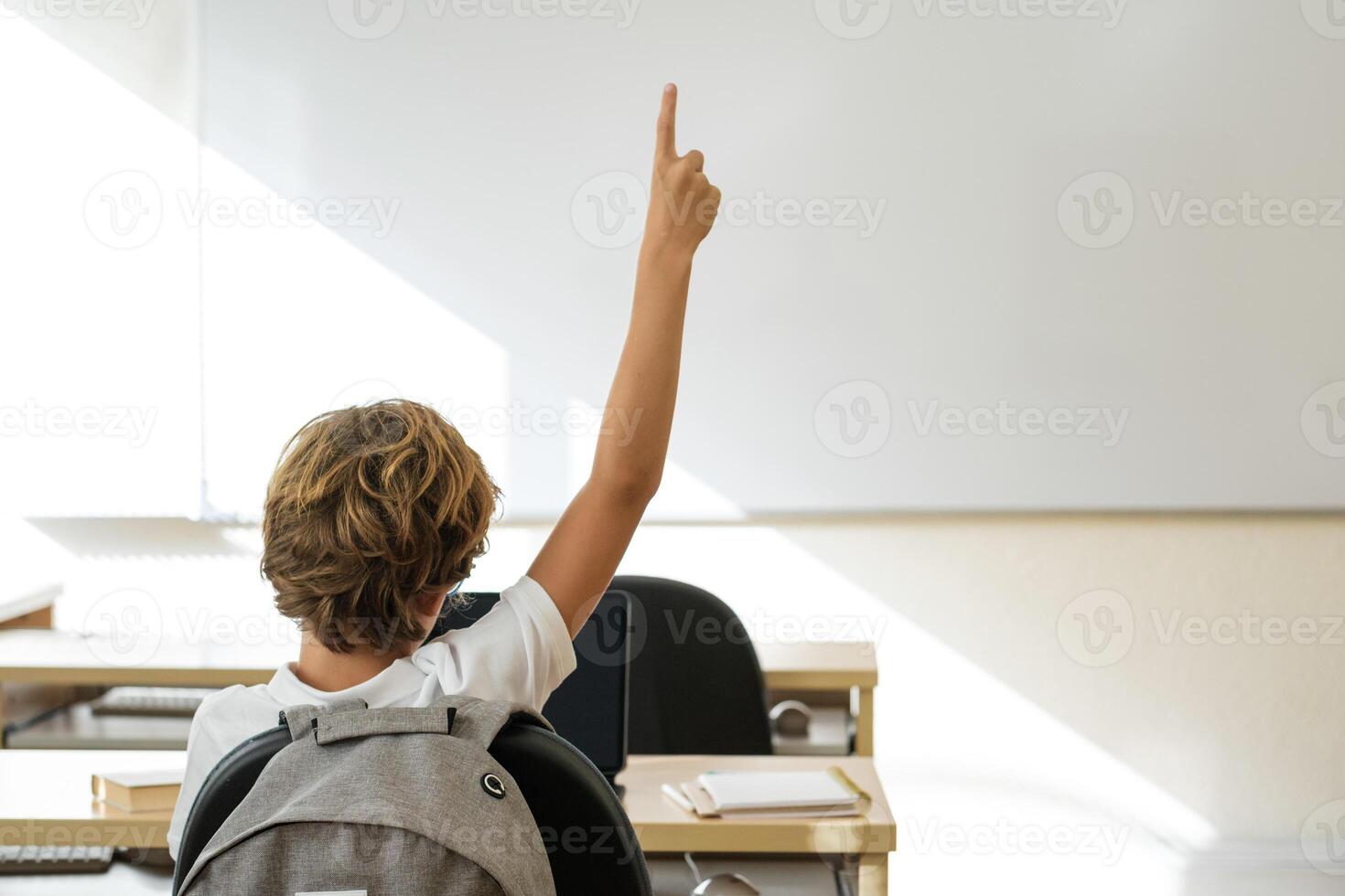 Schoolboy putting hand up in classroom at school photo