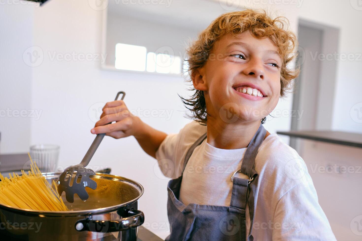 Positive boy cooking spaghetti in pot at home photo