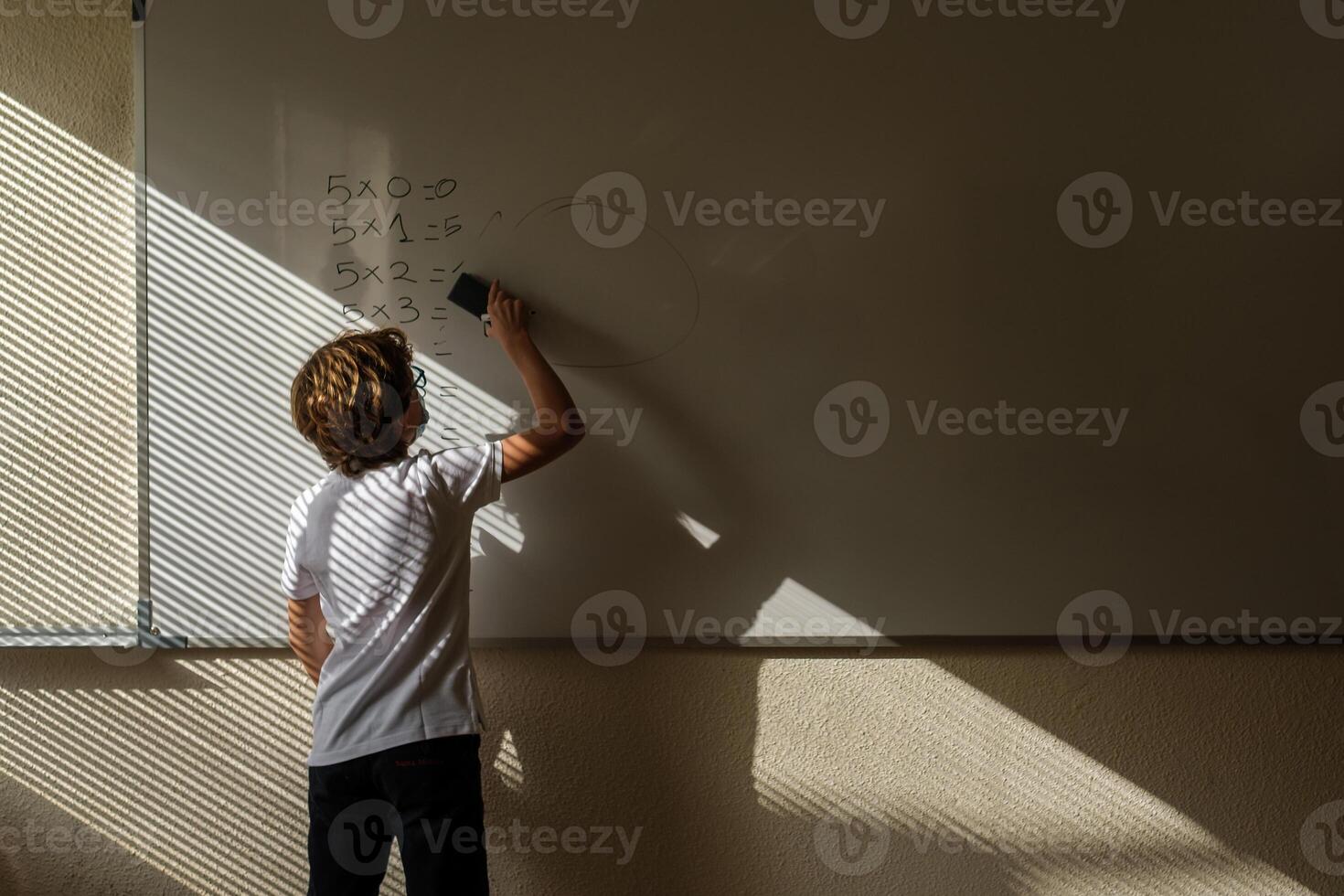 Unrecognizable schoolchild erasing math example from whiteboard photo