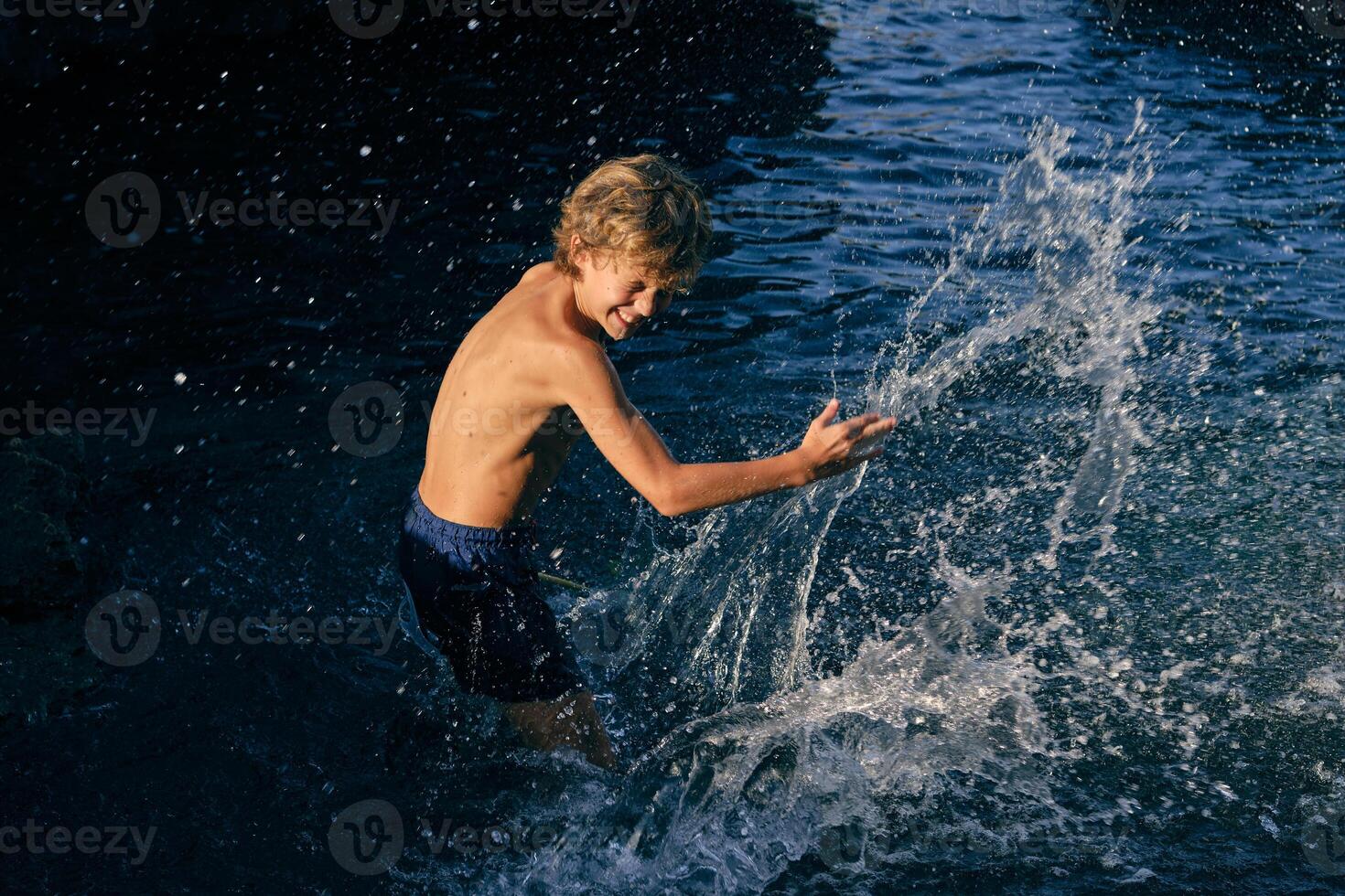 Cheerful boy having fun with splashing water in sea photo