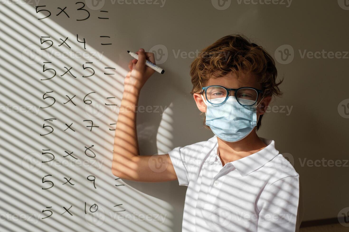 Schoolboy in mask writing on whiteboard during math lesson photo