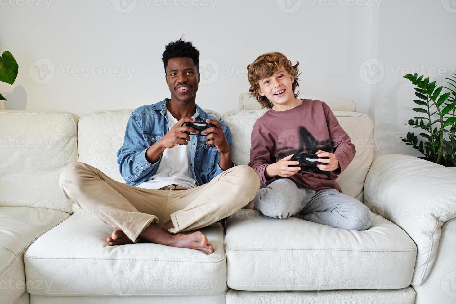 Cheerful diverse man and boy with gamepads resting on sofa photo