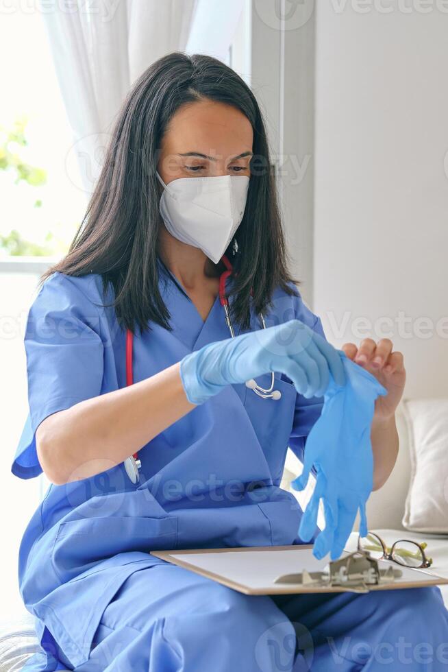 Physician in respiratory mask putting on disposable glove at hom photo