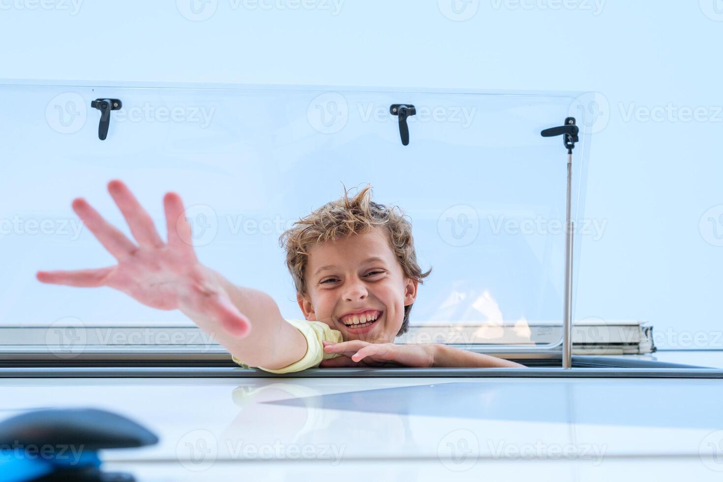 Boy smiling and reaching out from caravan window photo