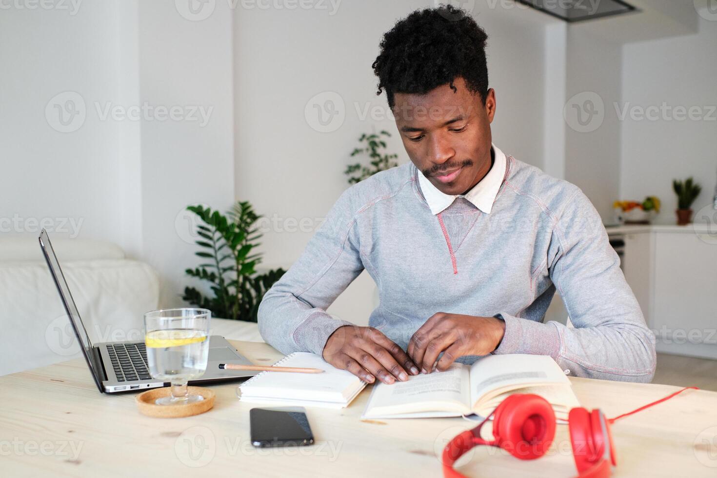 African American student reading book at table with laptop photo