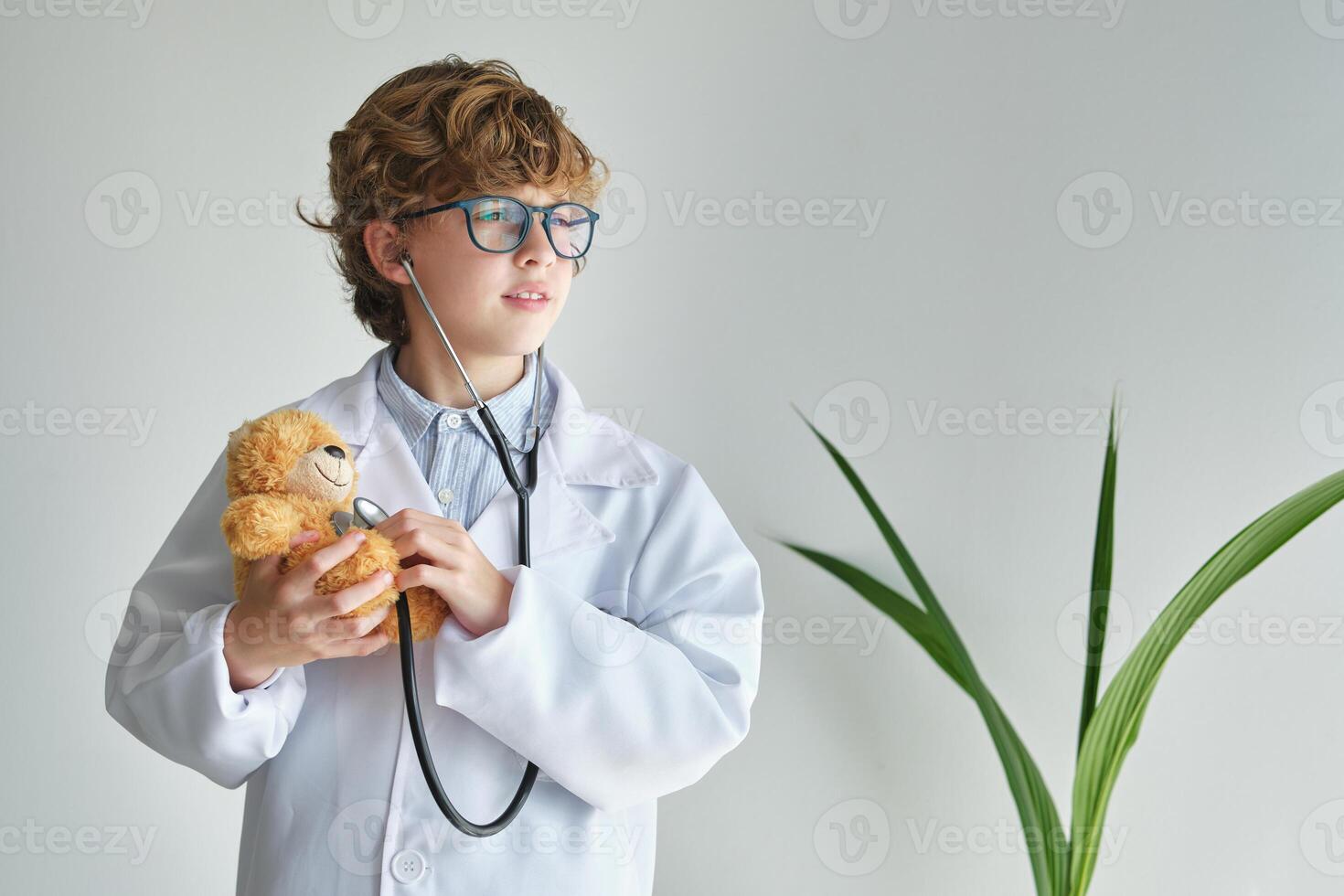 Dreamy boy in medical uniform examining toy bear with stethoscop photo