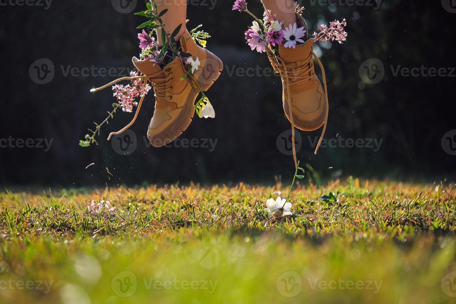 Crop person in boots with flowers jumping on grassy meadow photo