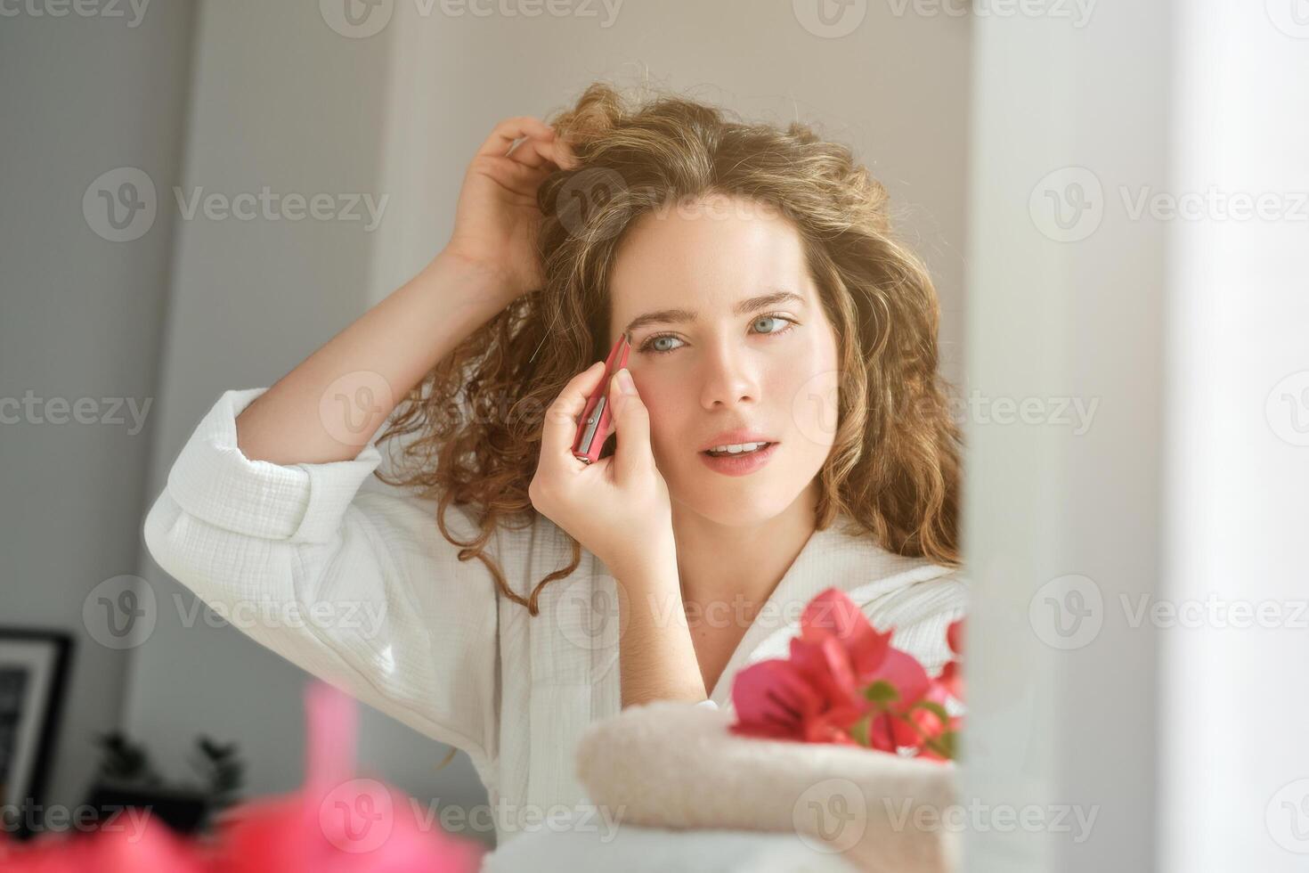 Woman tweezing eyebrows in front of mirror photo