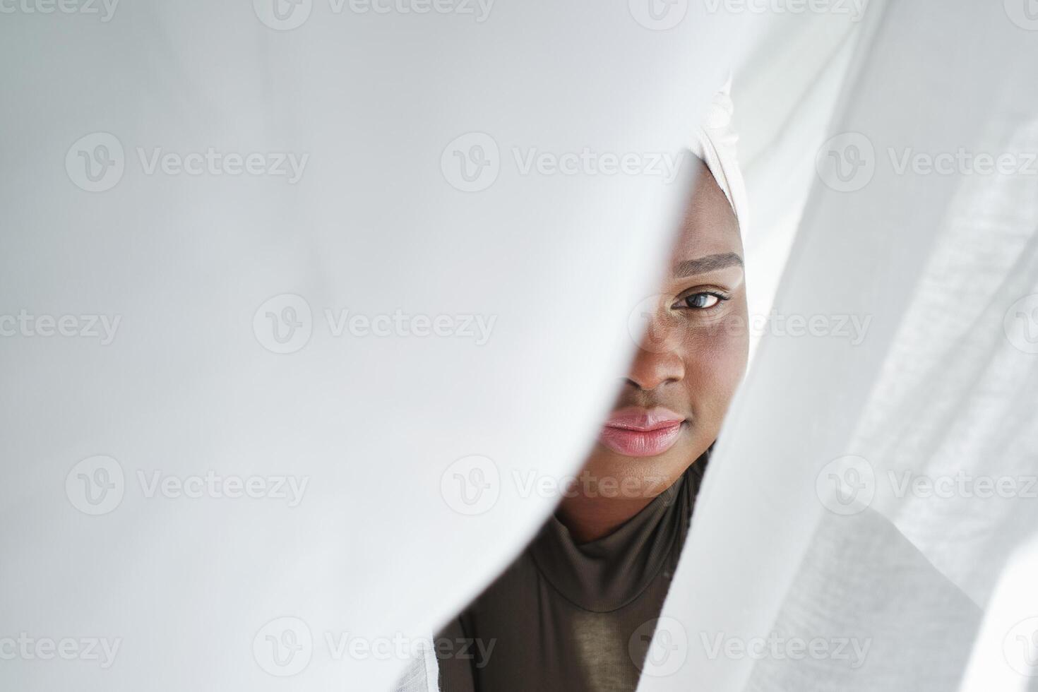 Black woman in headscarf with face covered with curtain photo