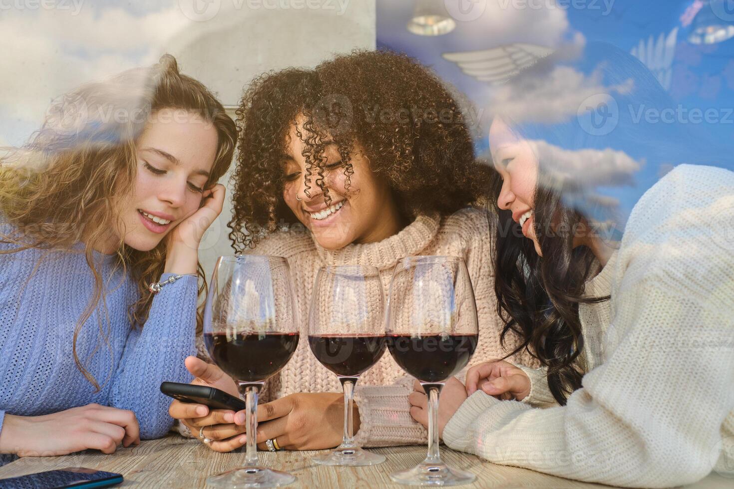 Smiling multiethnic ladies with wine looking at phone screen photo