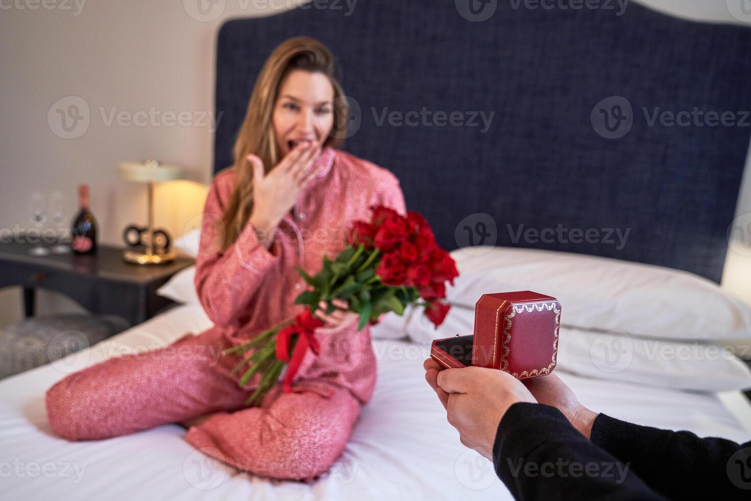 Woman with bouquet getting gift box on bed photo