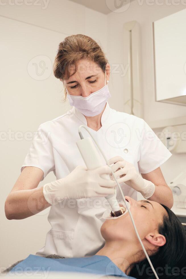 Dentist in mask scanning teeth of woman in dental clinic photo