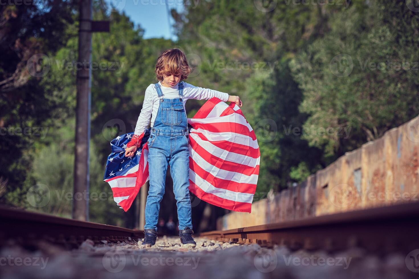 Preteen boy with waving American national flag standing on railr photo