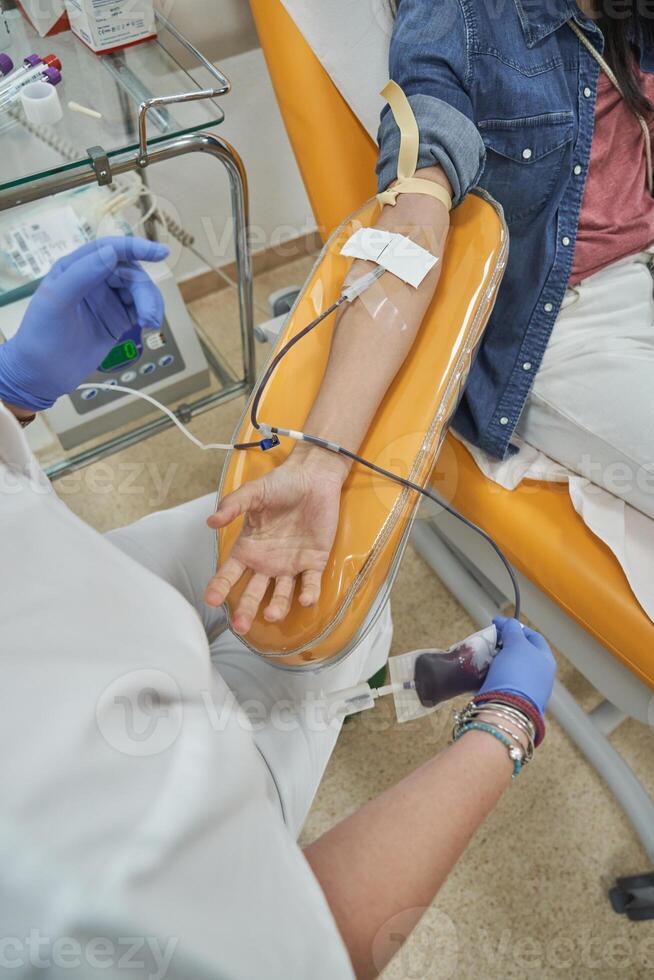 Crop nurse in scrubs performing blood donation on anonymous woma photo