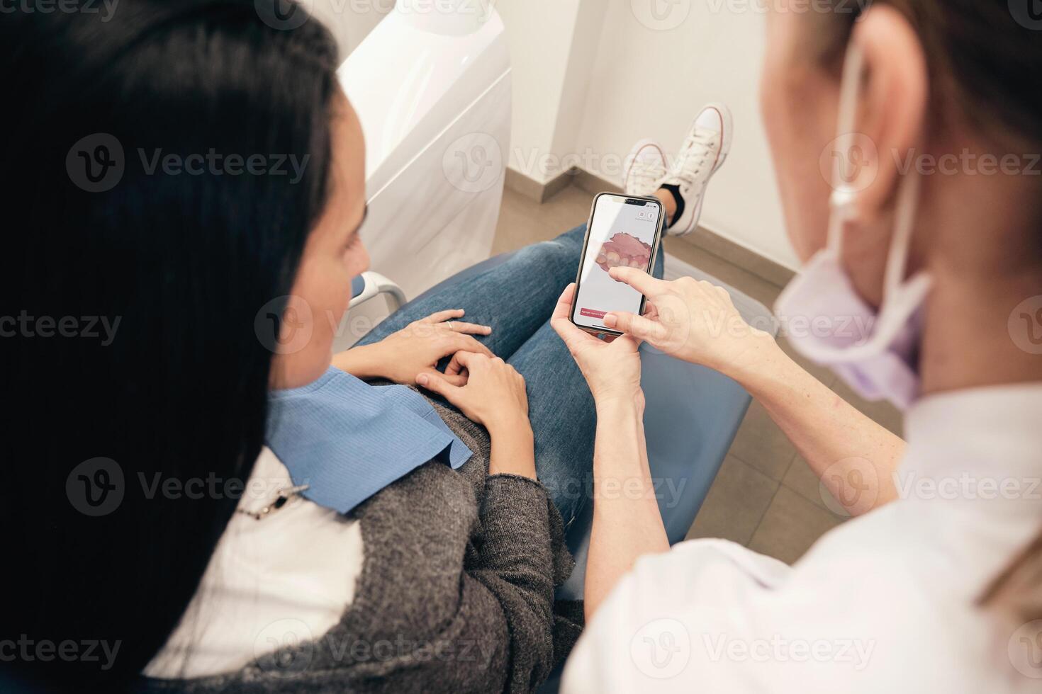 Crop orthodontist showing teeth scan on smartphone to female patient photo
