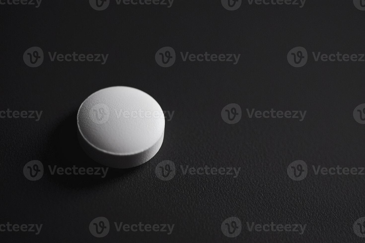 A single white round tablet rests on a matte black surface photo