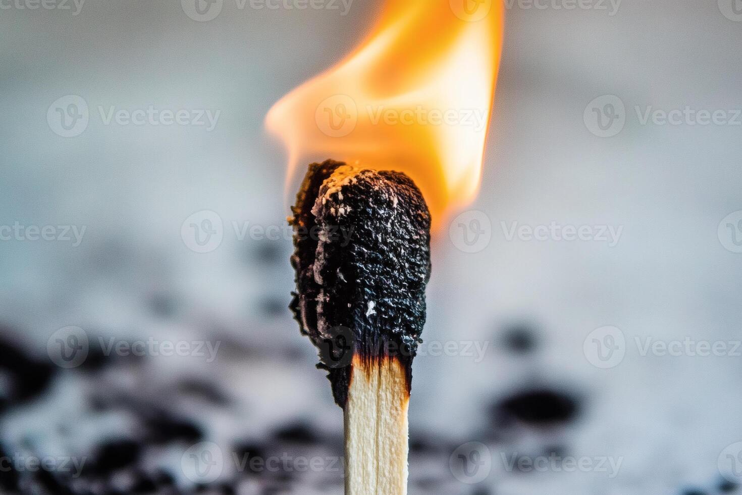 Burning matchstick creating a bright flame on a blurred background of ashes, representing fire and light photo