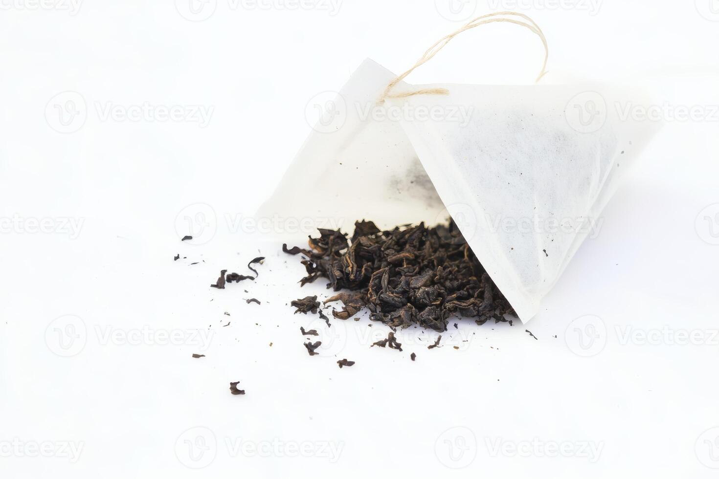 Loose black tea spills from a tea bag on a white surface. photo