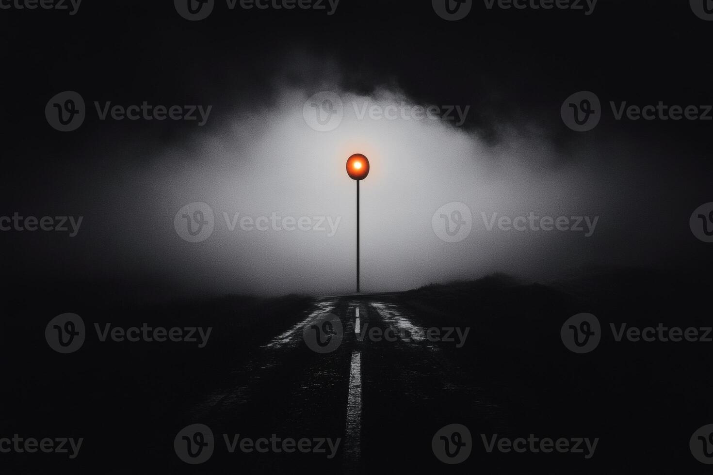 Lonely road illuminated by a solitary red light on a foggy night. photo