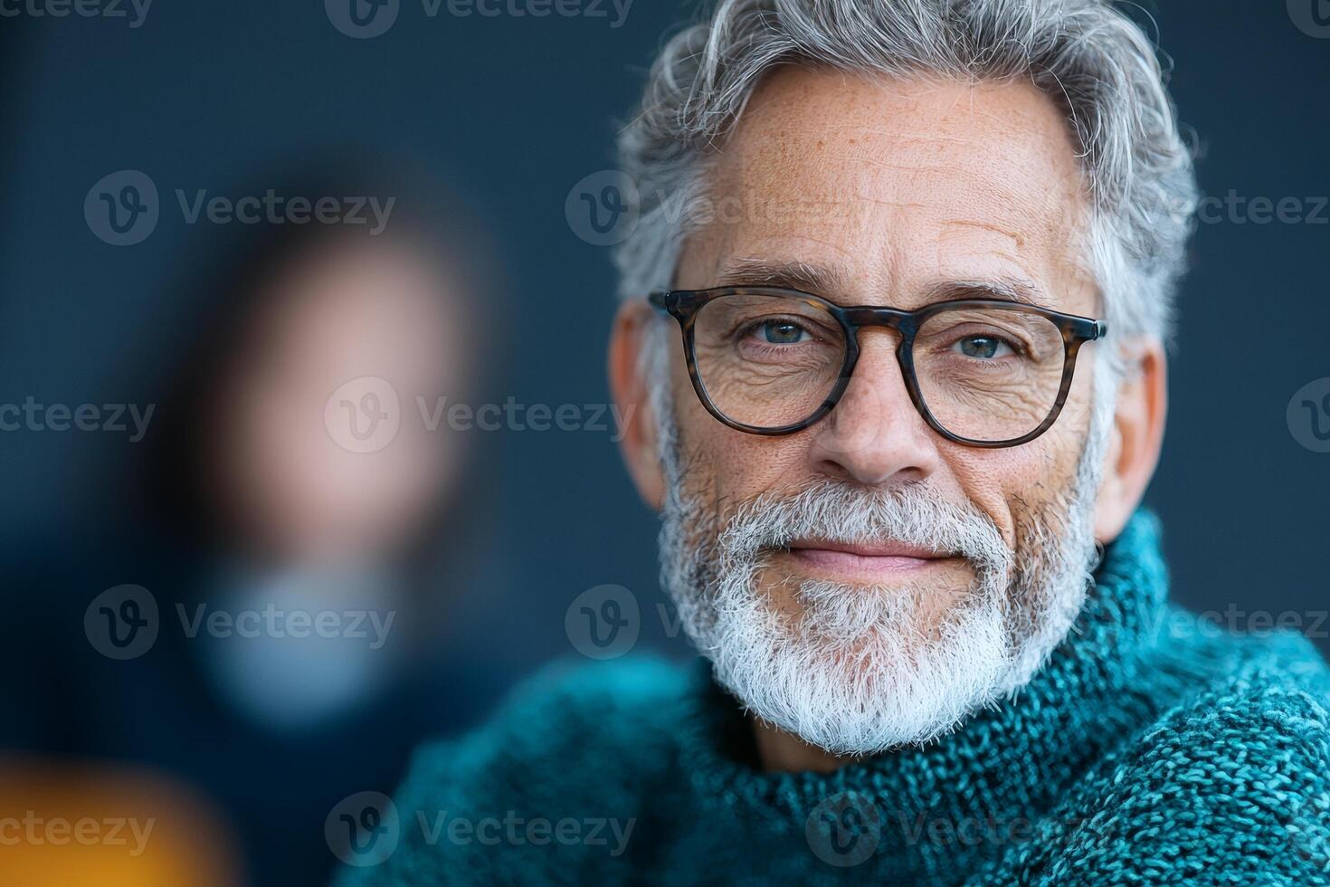 Portrait of a thoughtful older man wearing glasses, featuring a warm smile and cozy sweater against a softly blurred background photo