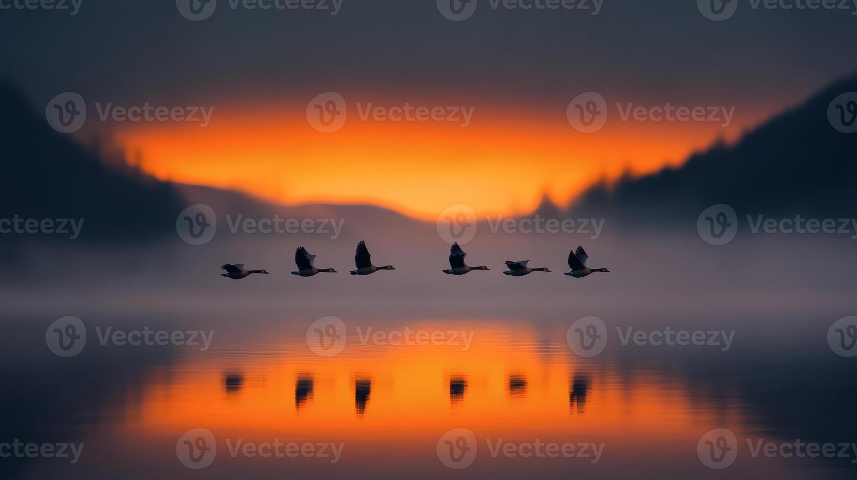 Wild geese soar elegantly above a tranquil lake at dusk, reflecting vibrant hues of orange and purple in the water photo
