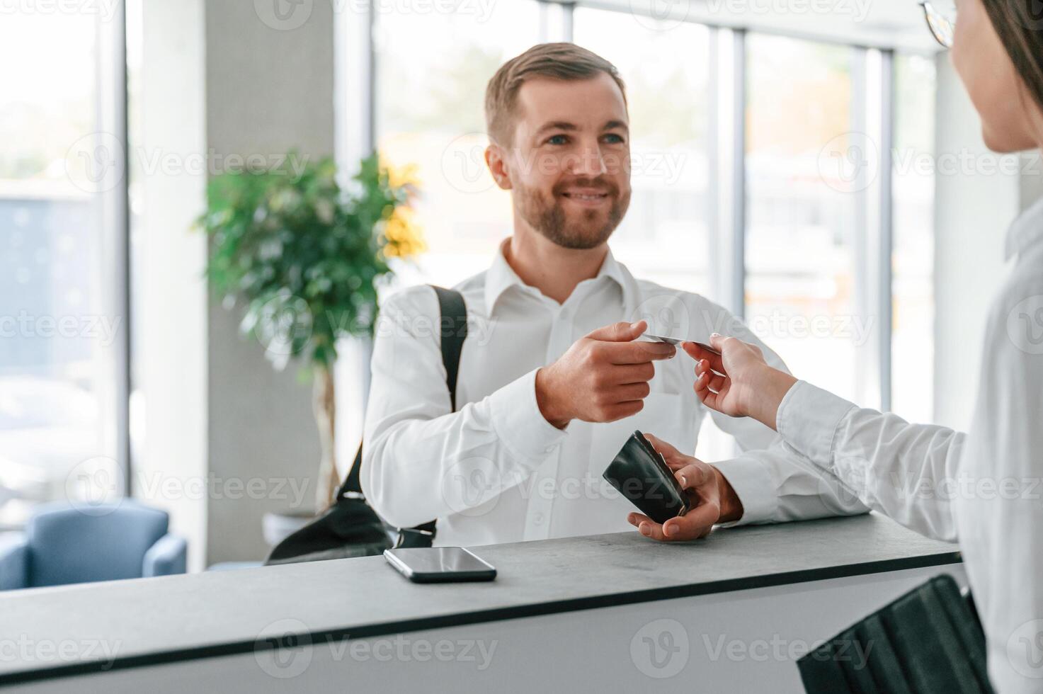 Assistant, helping customer. Man in white shirt is ordering a room in the hotel by woman's help photo