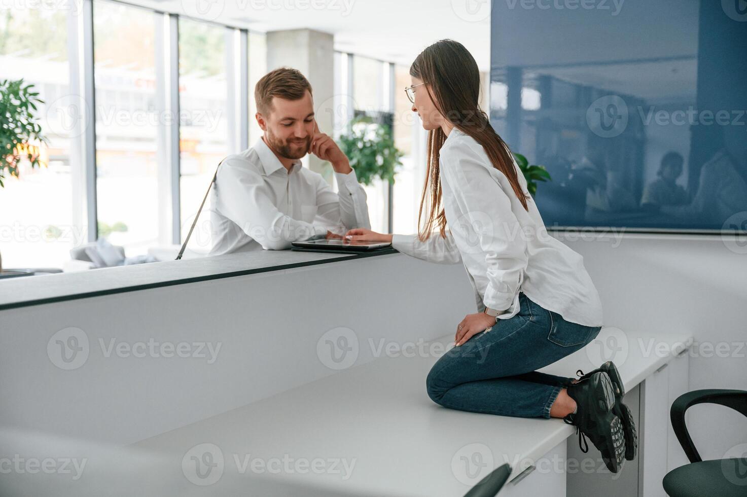 Woman sitting on the table on knees. Funny moment. Man in white shirt is ordering a room in the hotel by assistant help photo
