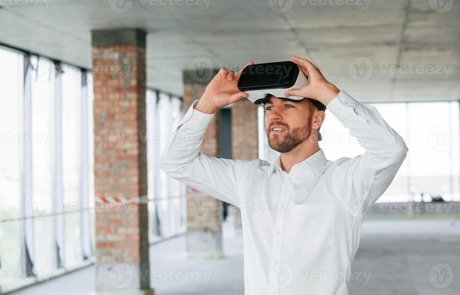 Man in, formal clothes is playing VR game, in the building that are on construction site photo