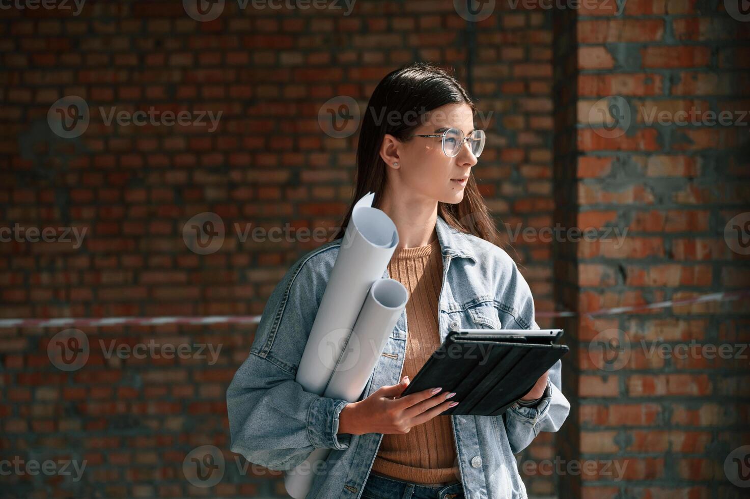 With plan in hands.. Young woman is standing in the unfinished building on construction site and working on a project photo