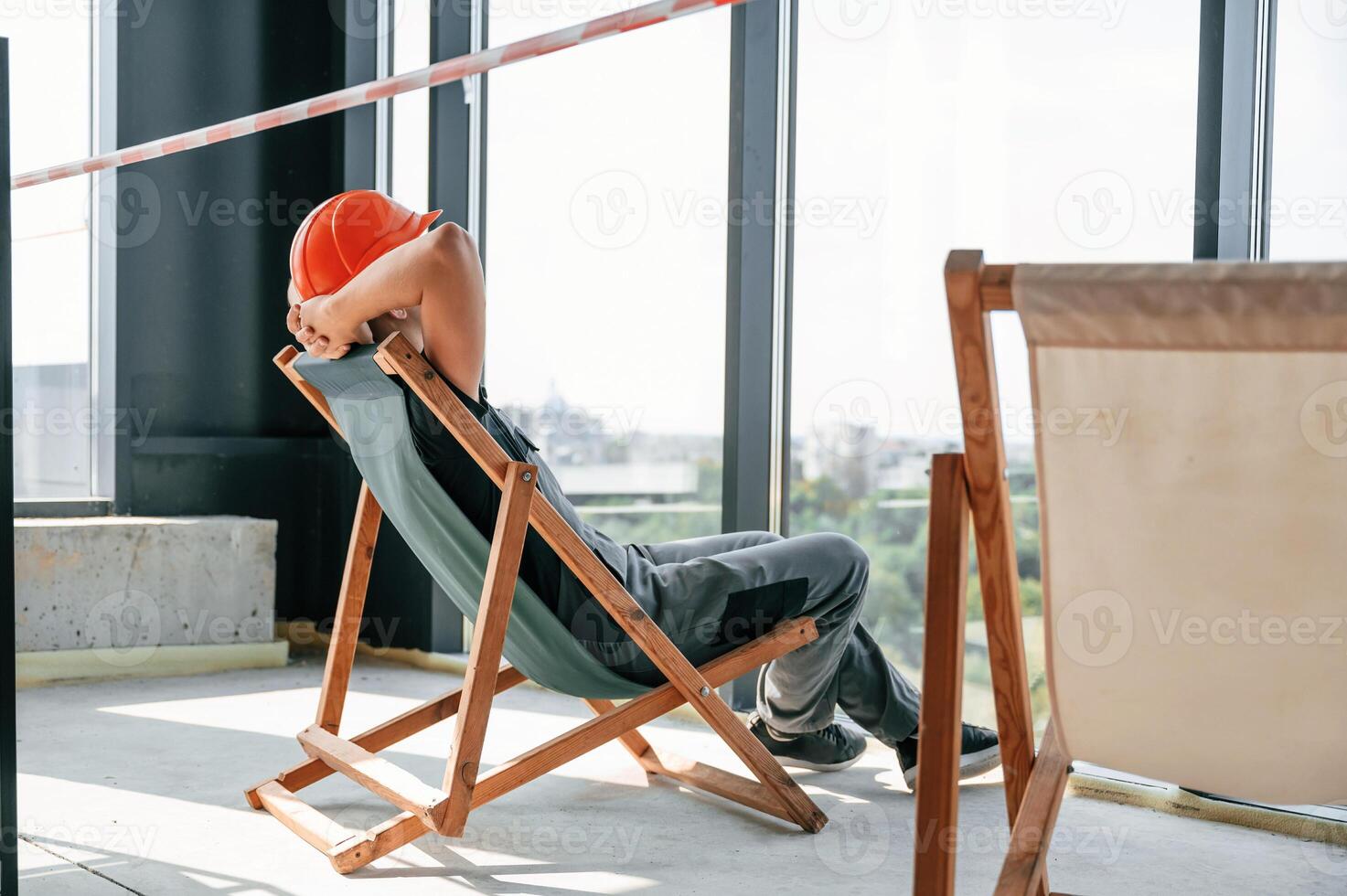 Foreman, in hard hat and uniform is sitting, looking at the view through windows while resting photo