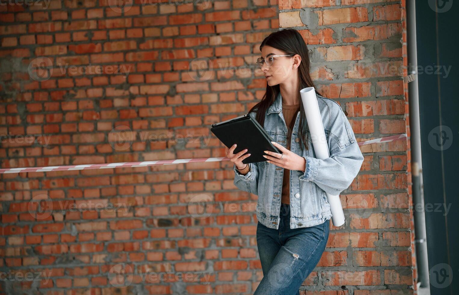Notepad in hands. Young woman is standing in the, unfinished building on construction site and working on a project photo