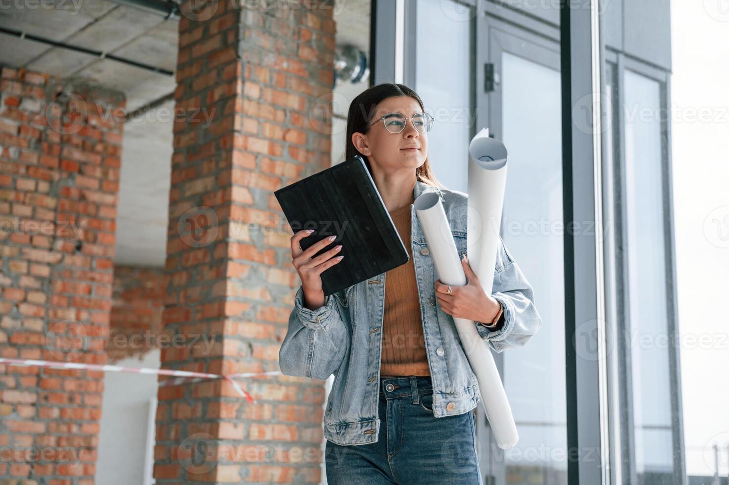 Young woman ,is standing in the unfinished building on construction site and working on a project photo