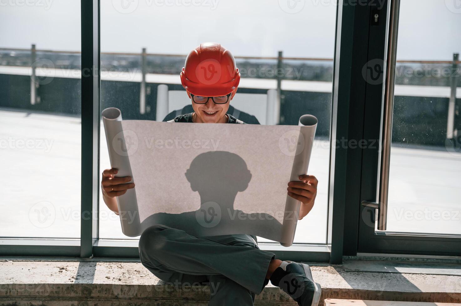 Foreman ,in hard hat is sitting indoors and reading plan of the building and construction photo