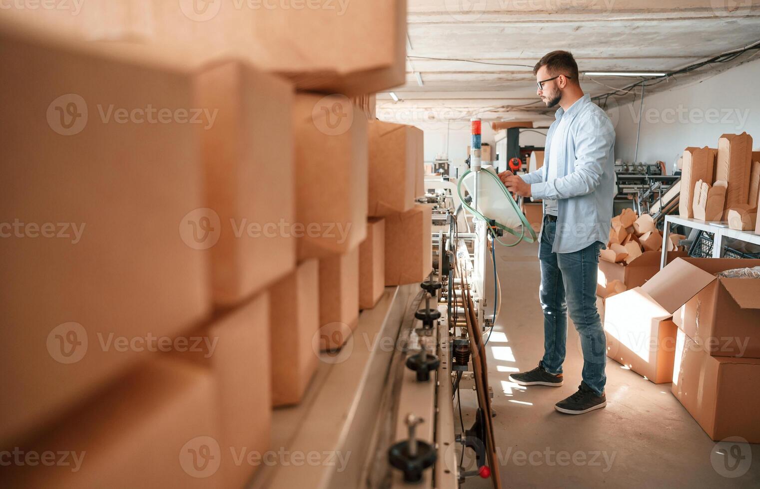 Machine operator is busy by setting up, a device. Print house worker in white clothes is indoors photo