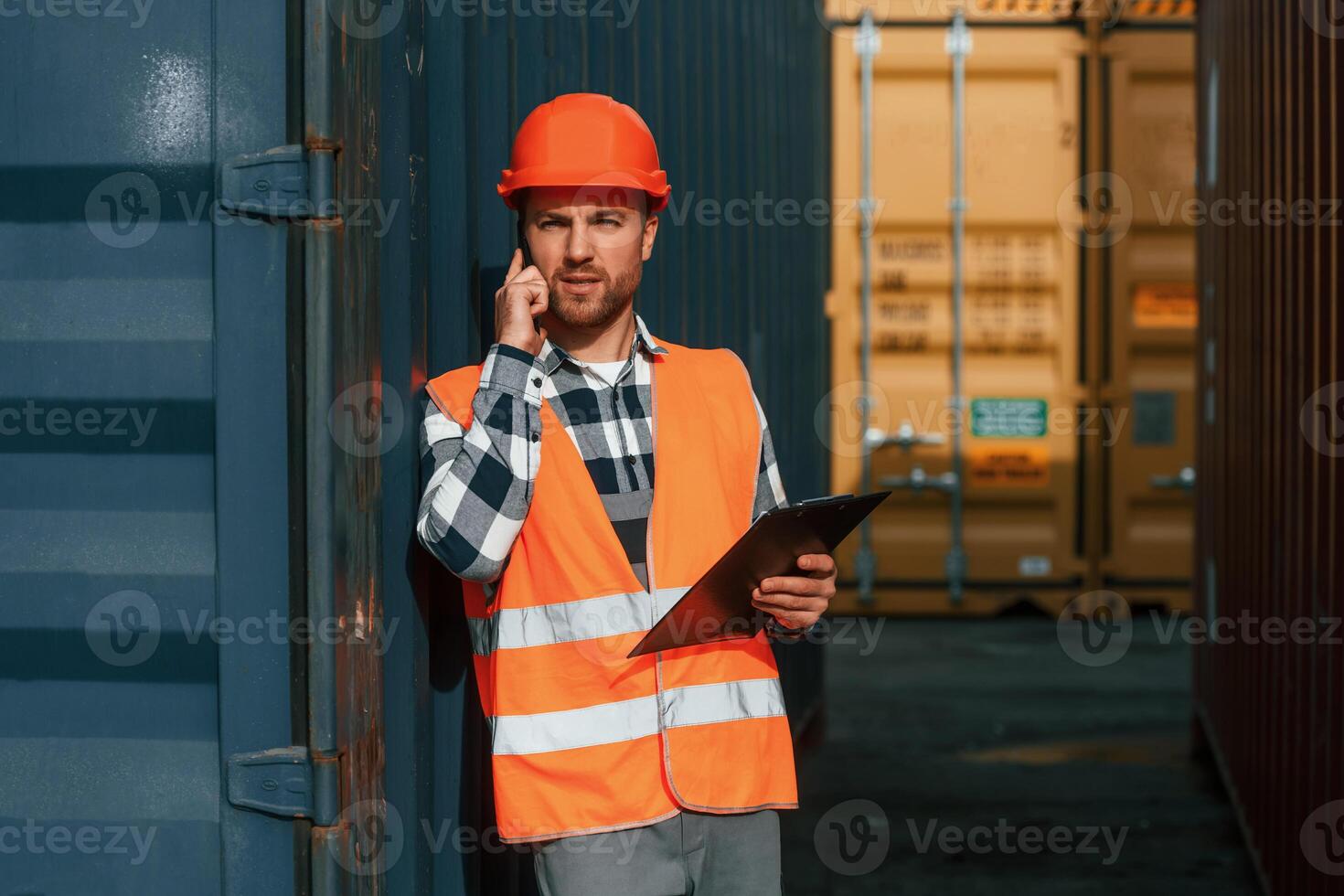 Using phone, and holding tablet. Male worker is on the location with containers photo